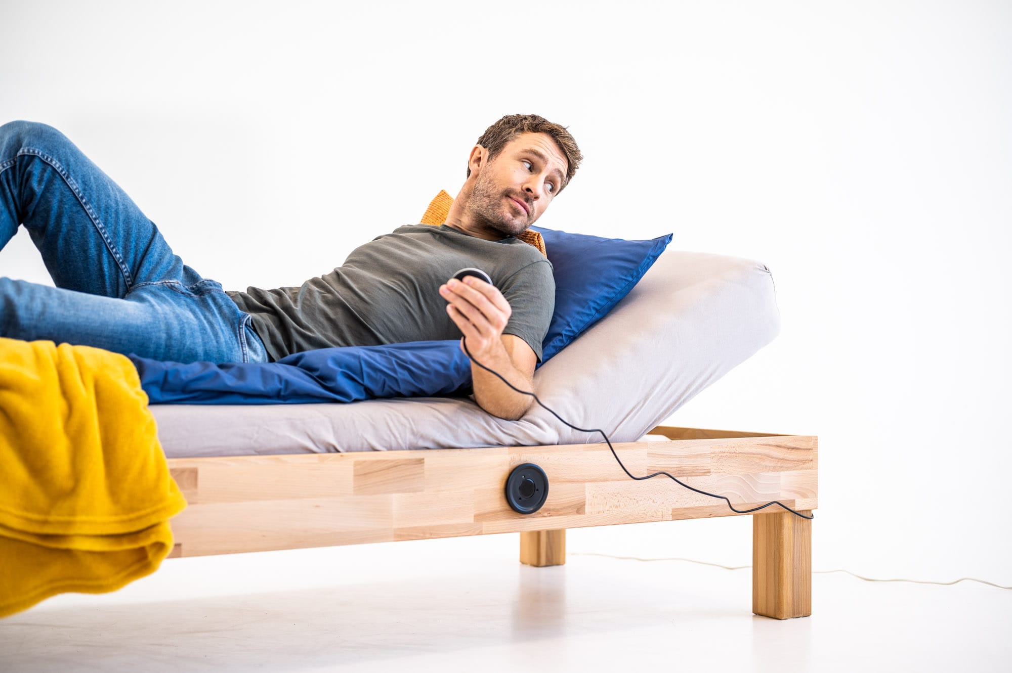 Mann liegt auf einem Bett mit dem CosyLift und steuert die elektrische Verstellung der Matratze mit einer Fernbedienung