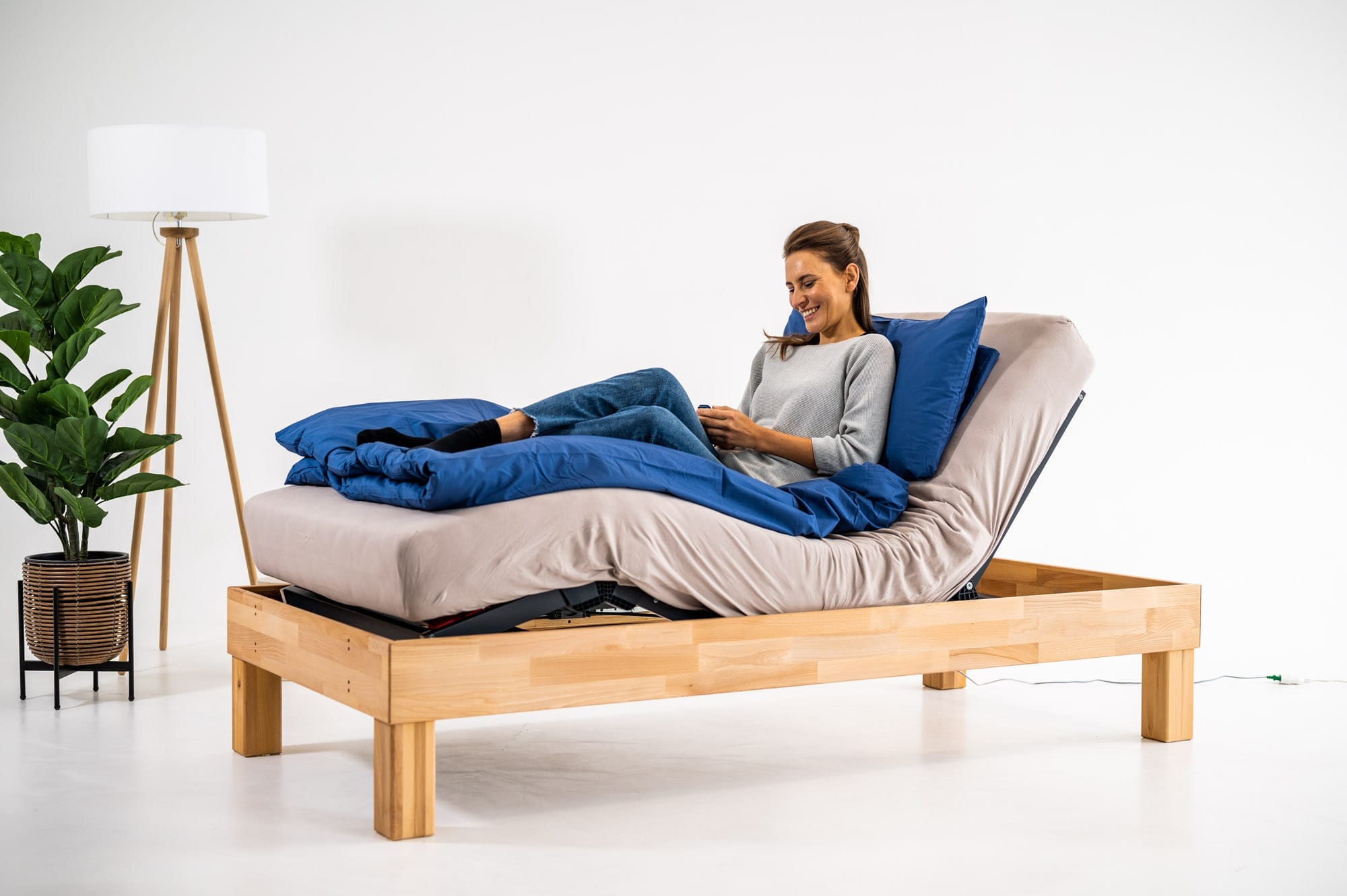 Frau liegt auf einem Bett mit klassischem elektrischem Lattenrost und hebt die Liegefläche per Motor an