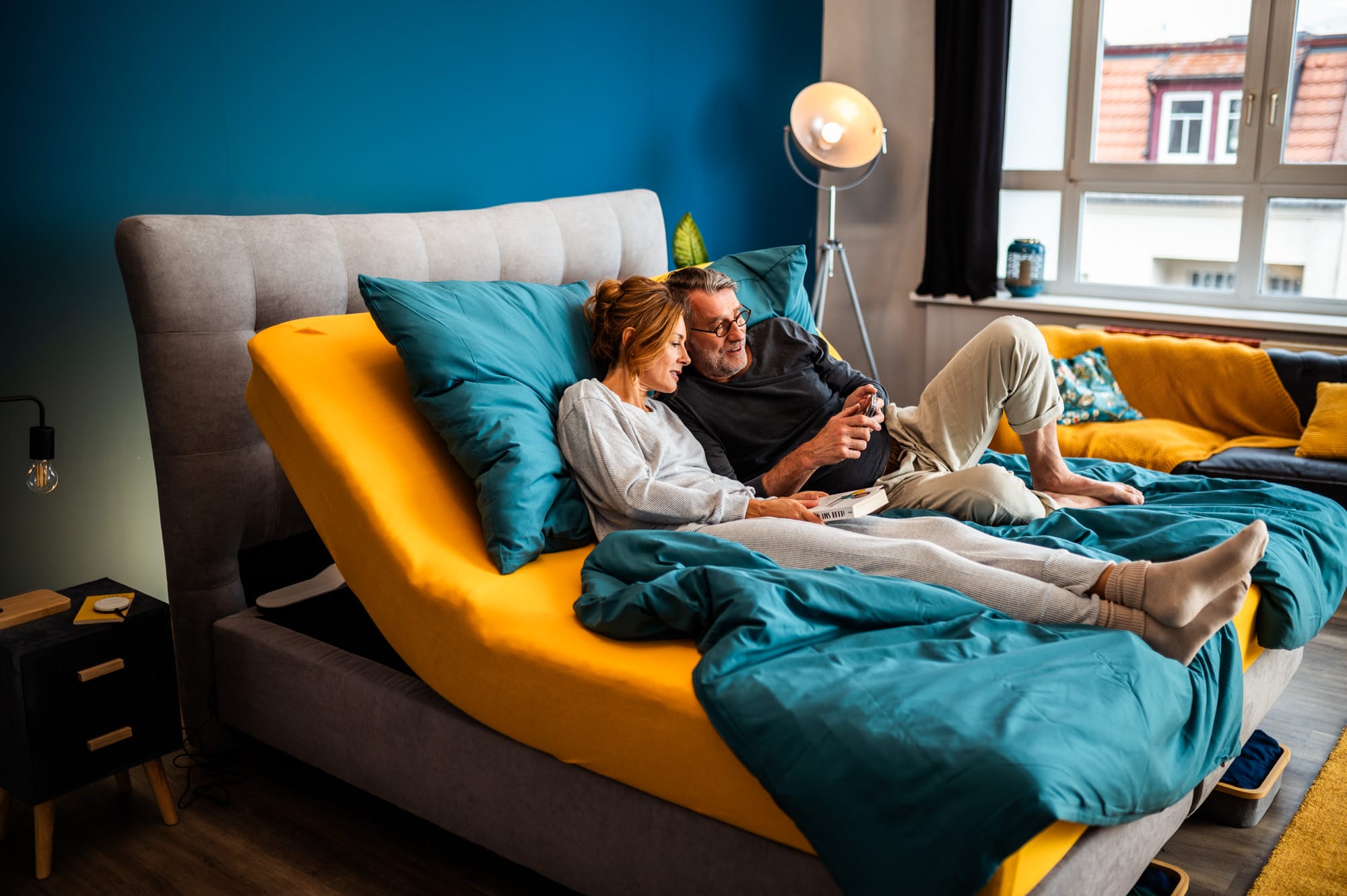 Paar liegt auf einem Bett mit dem CosyLift, der die Matratze elektrisch anhebt und eine bequeme Sitzposition ermöglicht