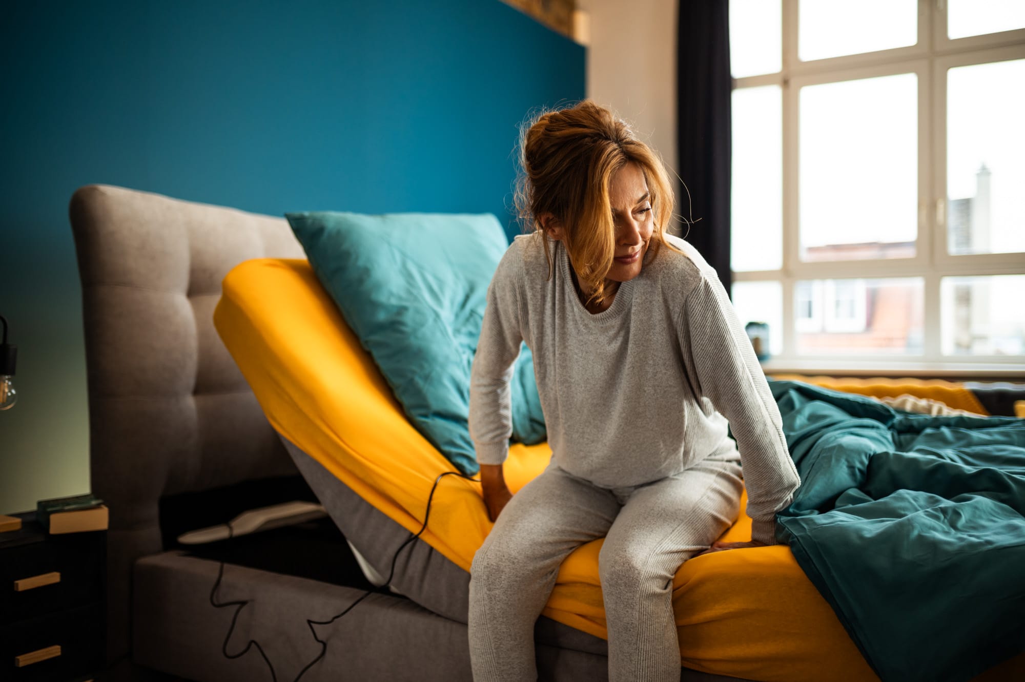 Ältere Frau sitzt auf einem Bett mit dem CosyLift, der die Matratze elektrisch anhebt und das Aufstehen erleichtert