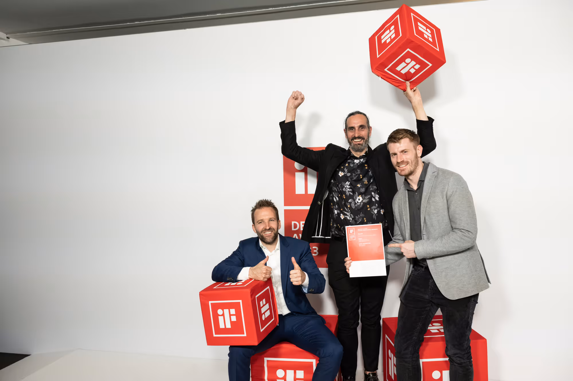 Drei Männer feiern mit Urkunde und roten iF-Design-Award-Würfeln den Gewinn des iF Design Award 2023 für den CosyLift.