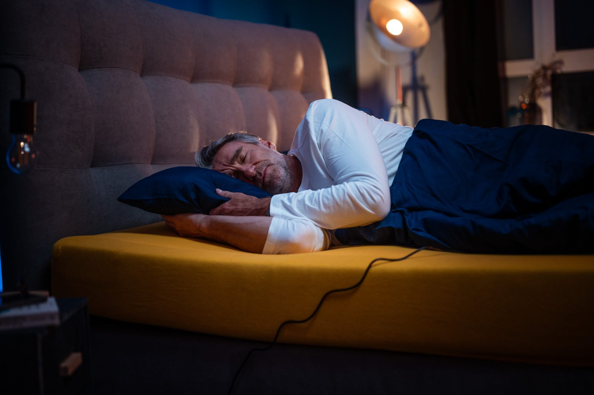 Mann schläft seitlich auf einer Matratze in dunkler Schlafzimmerumgebung und wirkt entspannt.